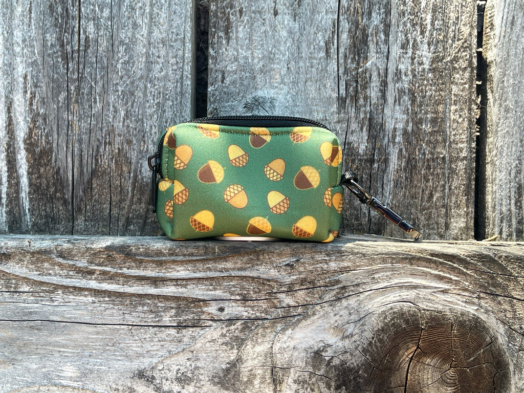 Handmade neoprene dog waste bag dispenser with green acorn pattern, shown in use outdoors. Securely attaches to leash for easy waste disposal.