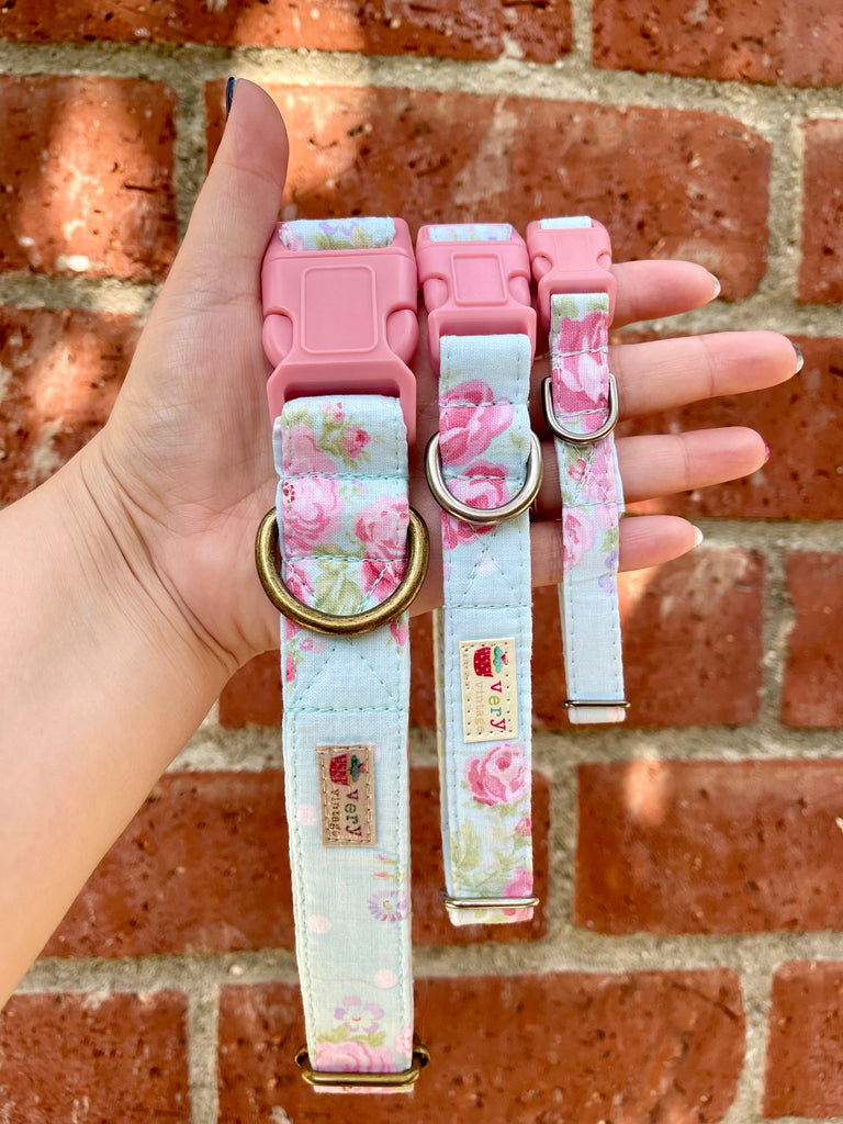 Three handmade floral dog collars in rose print held in hand with red brick wall backdrop.