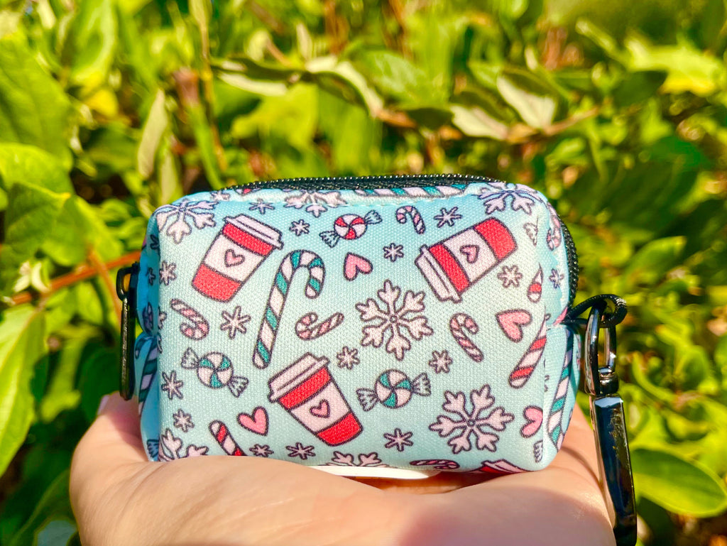 Festive Peppermint Mocha poop bag holder with holiday coffee and candy print, held in hand with leafy greenery in background.