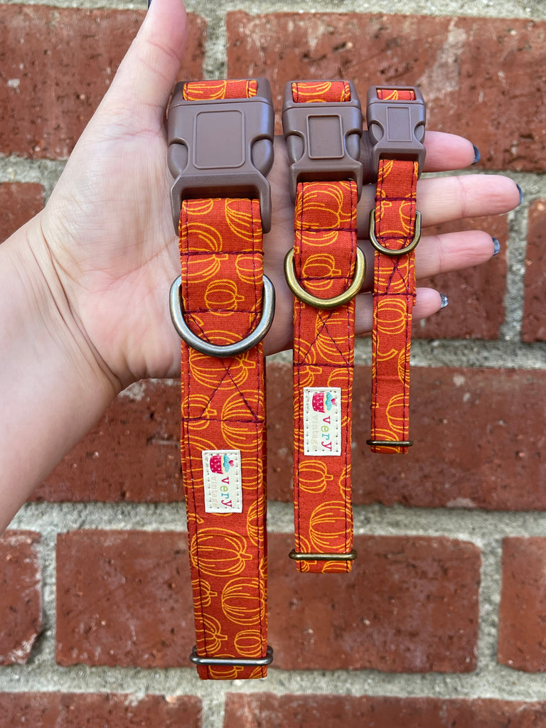 Handmade pumpkin print dog collars with brown buckles against brick background