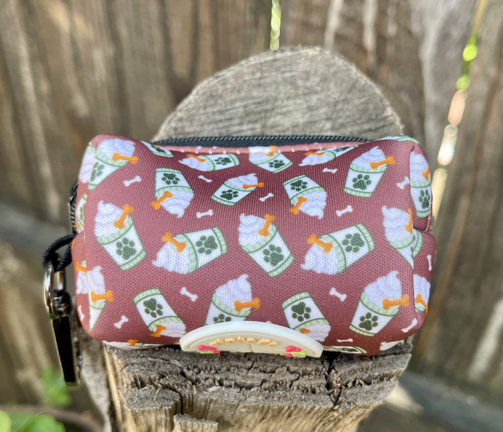 Puppachino poop bag holder resting on tree stump with zipper and black metal clip visible