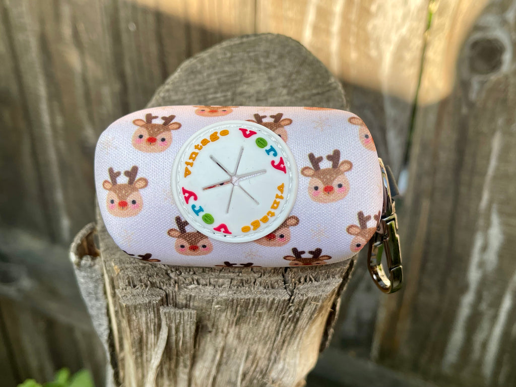Close-up of the dispenser port on the back of the reindeer poop bag holder, surrounded by smiling reindeer on a white background