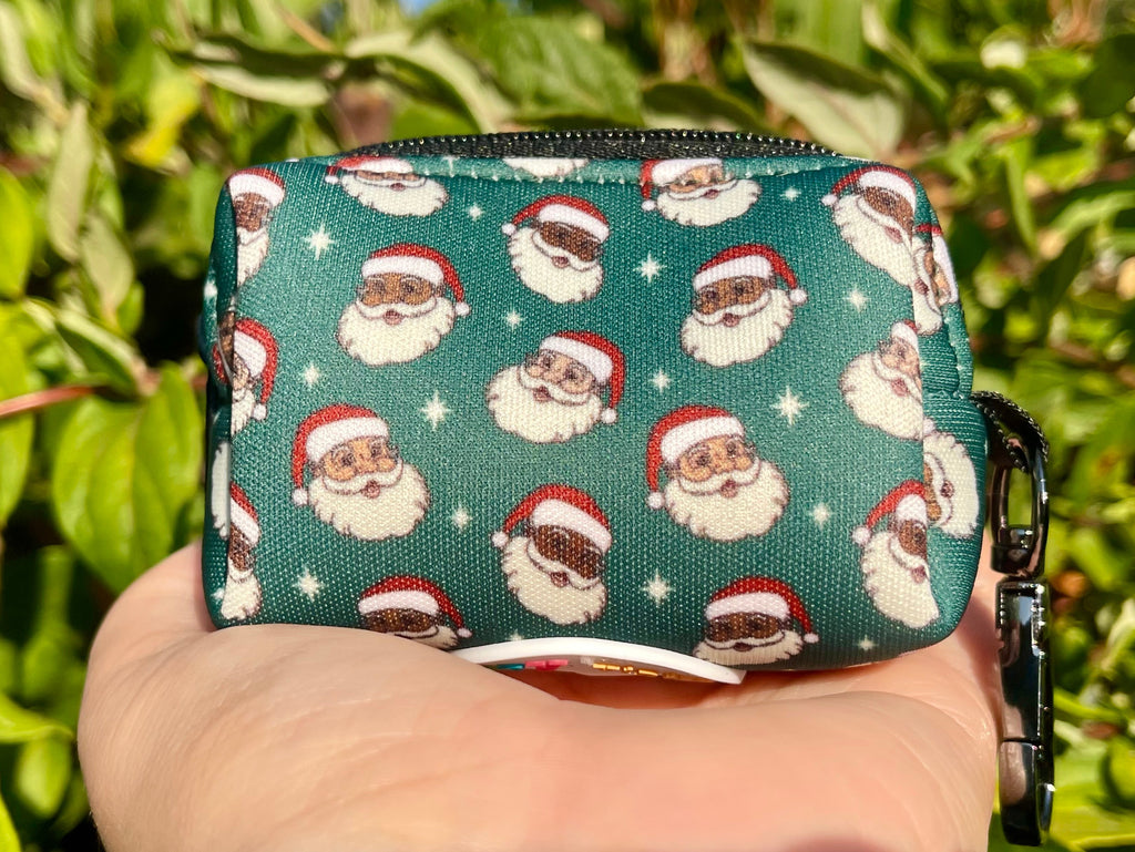 Green Santa Claus poop bag holder shown in hand with leafy outdoor background and sunlight