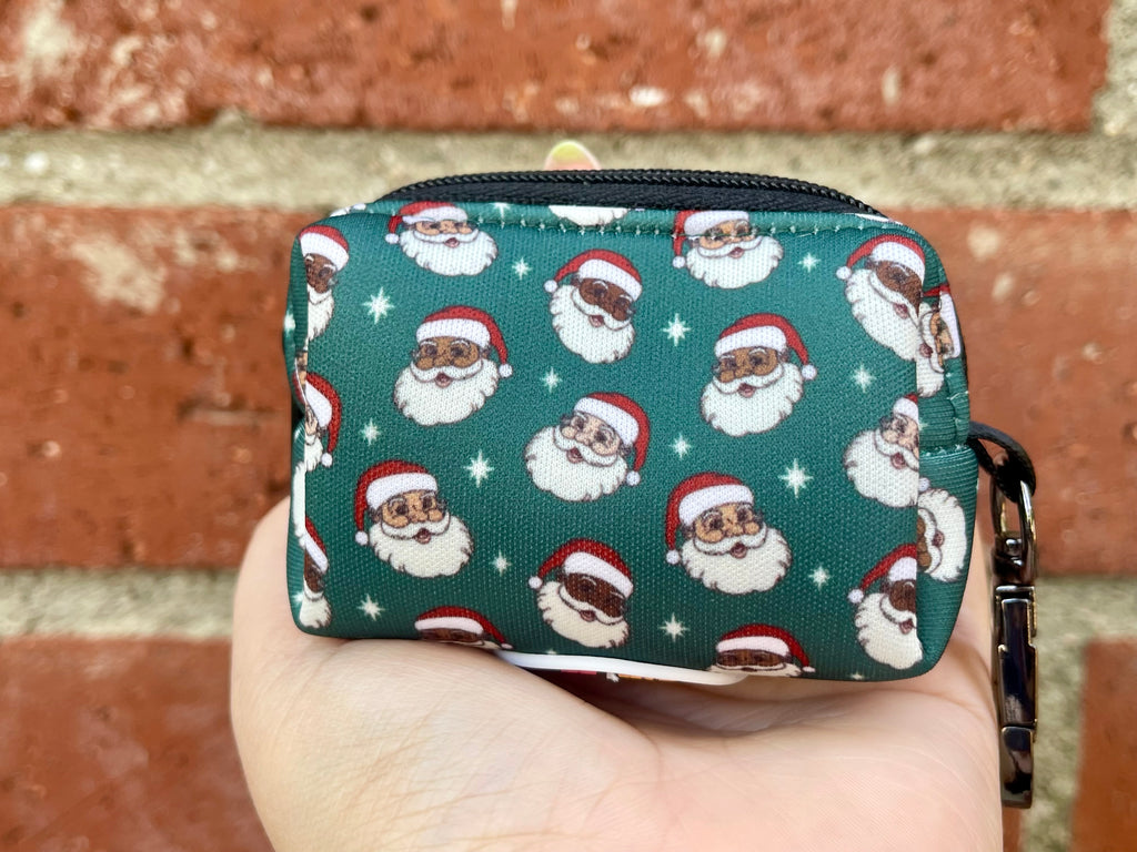 Holiday-themed poop bag holder with Santa print, displayed in hand against red brick wall