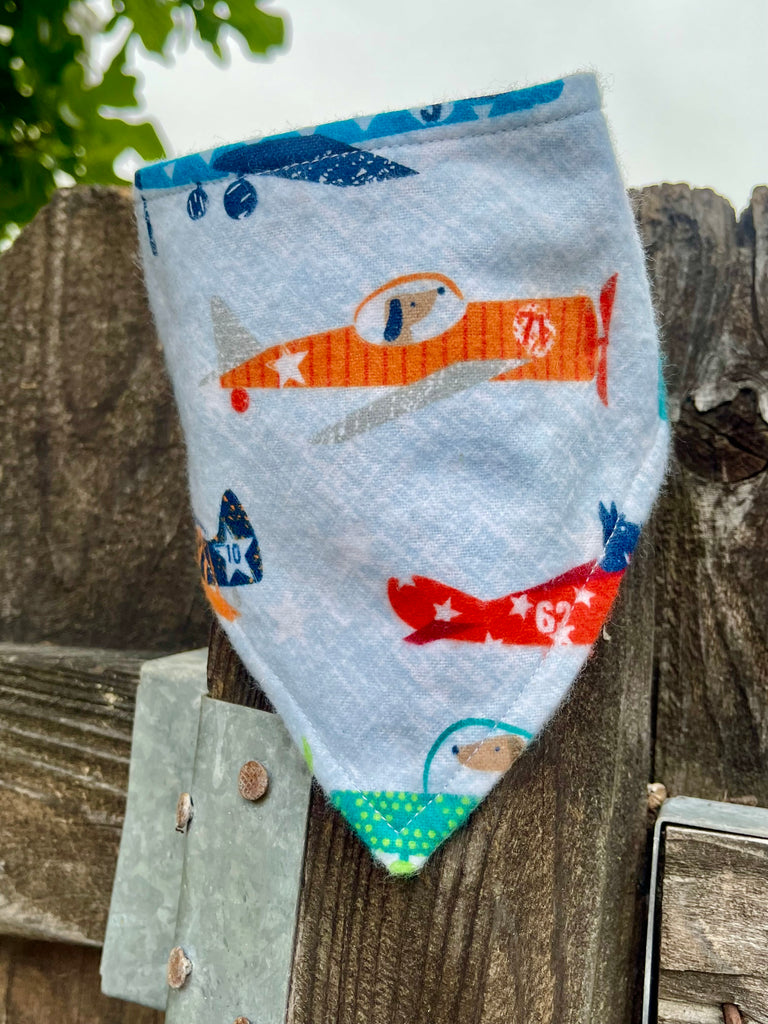 Snap-on dog bandana with retro airplane design displayed on a wood fence