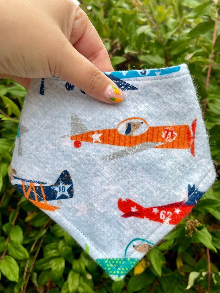 Top Paw dog bandana featuring planes and dogs held in front of leafy background