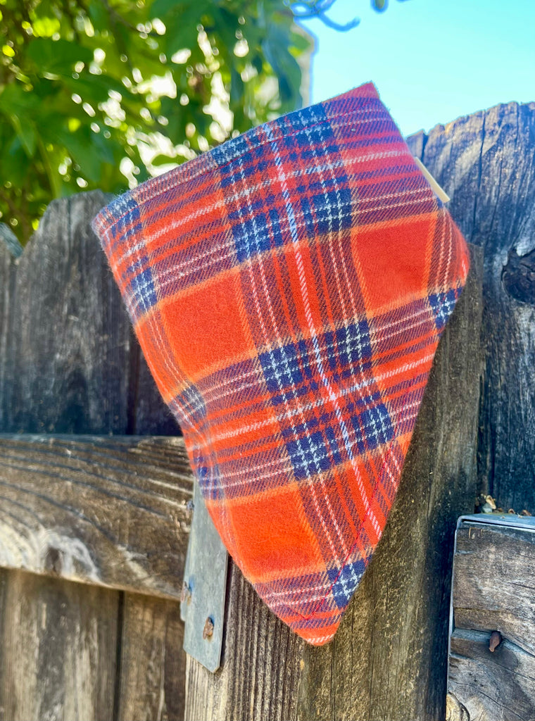 Orange plaid dog bandana draped on rustic wood fence, eco-friendly fall pet scarf handmade in USA