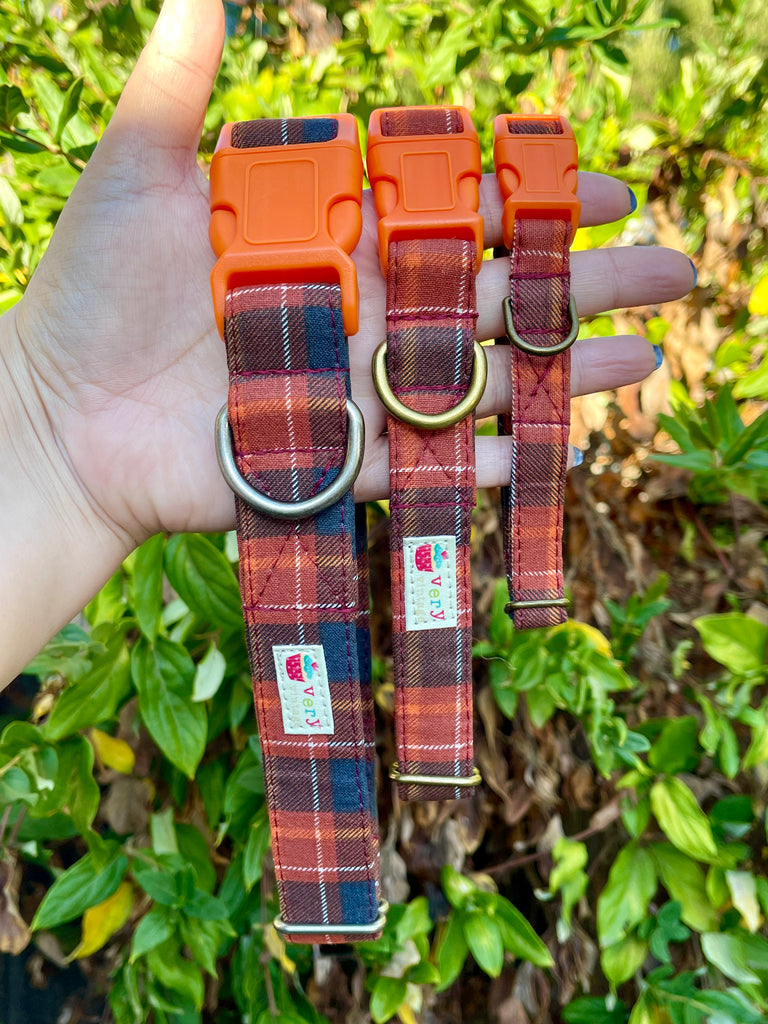 Hand holding handmade orange and navy plaid dog collars outdoors