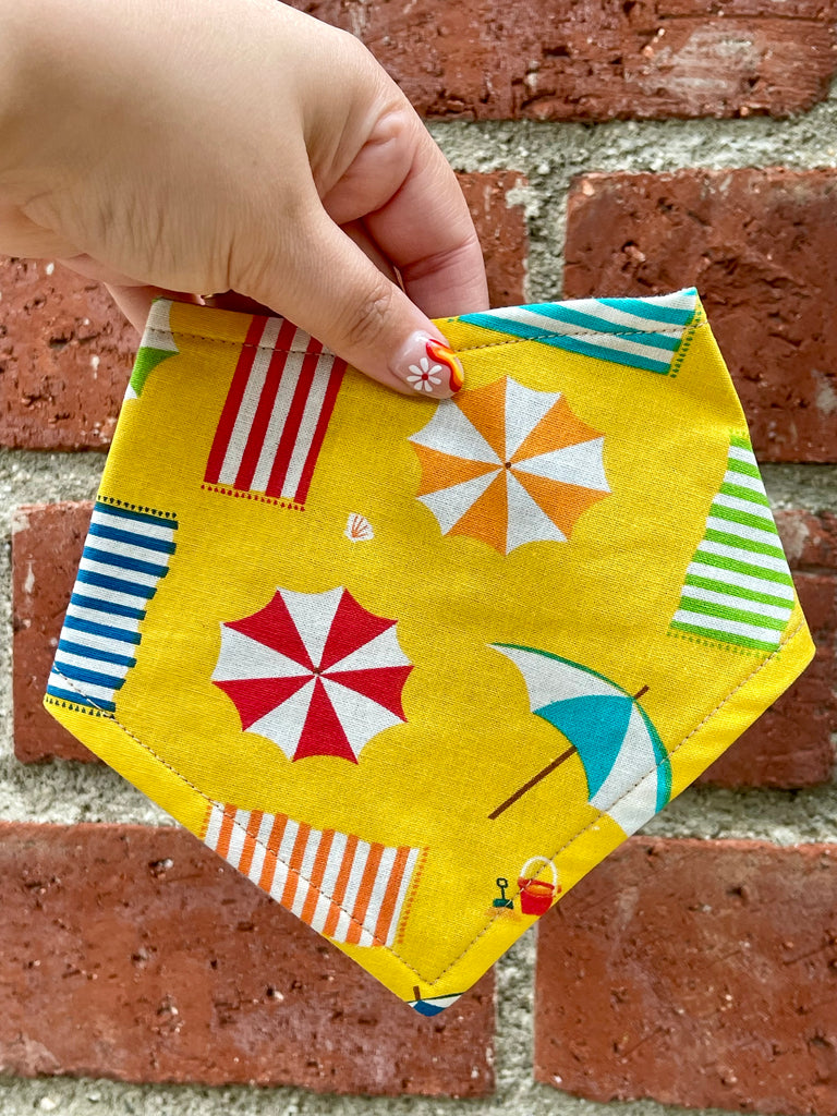 Close-up of yellow beach-themed snap-on bandana for dogs and cats, organic cotton fabric, shown on rustic brick backdrop, handmade in Los Angeles.