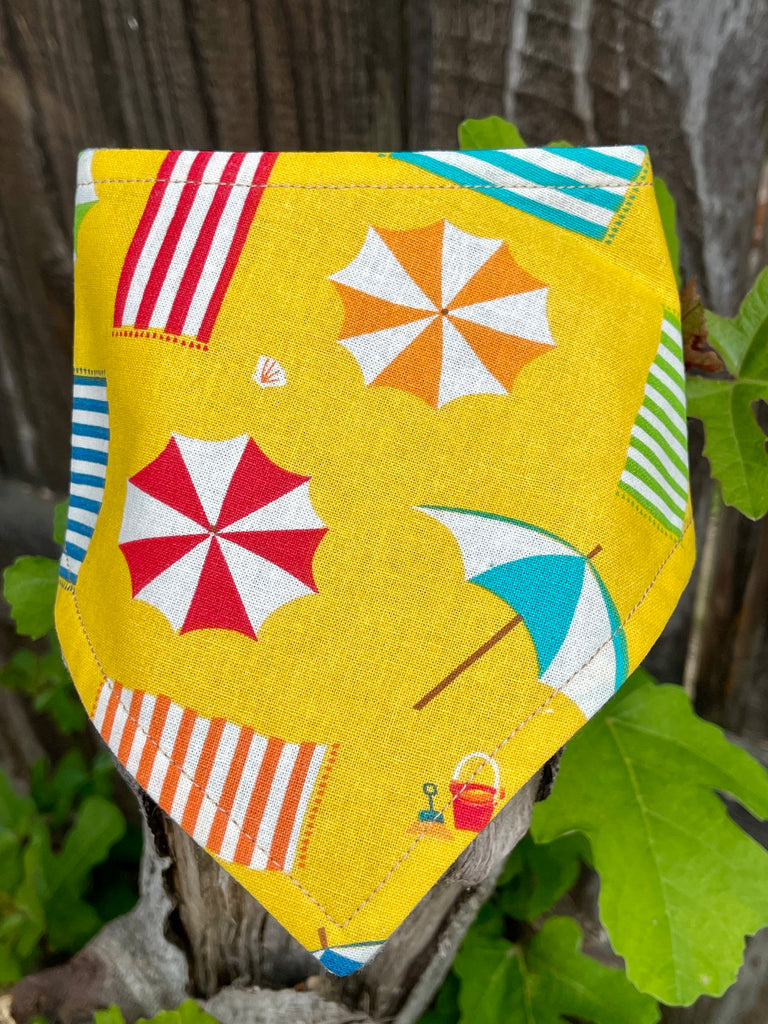 Soft yellow dog bandana with playful beach pattern, folded and laid flat on a stump for a detail view, perfect eco-friendly pet neckwear.