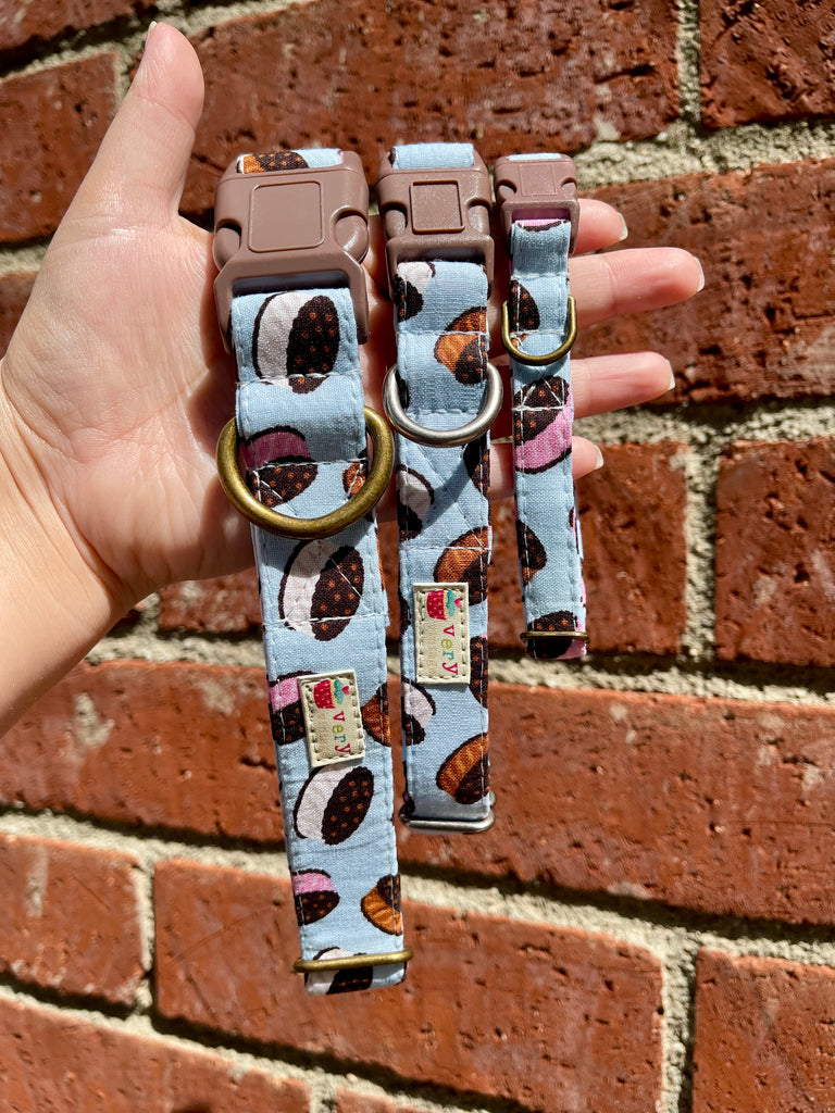 Light blue dog collar featuring chocolate, vanilla, and strawberry ice cream sandwich prints, displayed on hand with vintage brick background, perfect for a cheerful, summer-themed pet look.