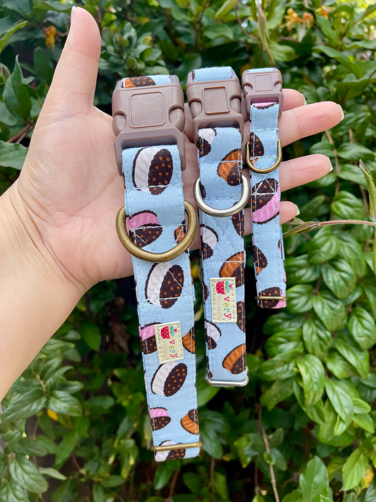 Light blue dog collar with chocolate, vanilla, and strawberry ice cream sandwich design, shown on hand against lush green ivy background, evoking a fun and playful summer vibe.