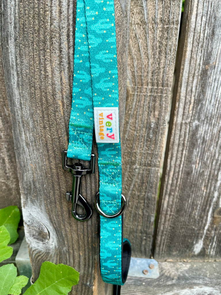 Teal cactus print leash clipped to a wooden fence, showing the black metal clip and D-ring