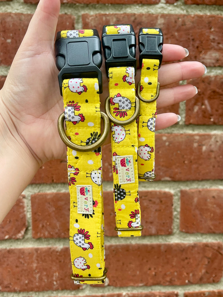Yellow chicken print dog collar with black buckle, held in hand against vintage red brick wall – handmade in Los Angeles