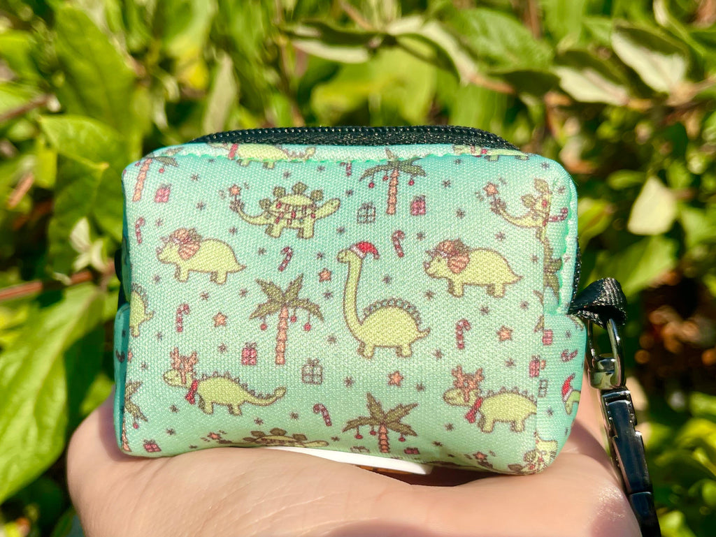 Christmas Dinos poop bag holder held in hand outdoors – bright lighting highlights the festive pattern against a green garden background