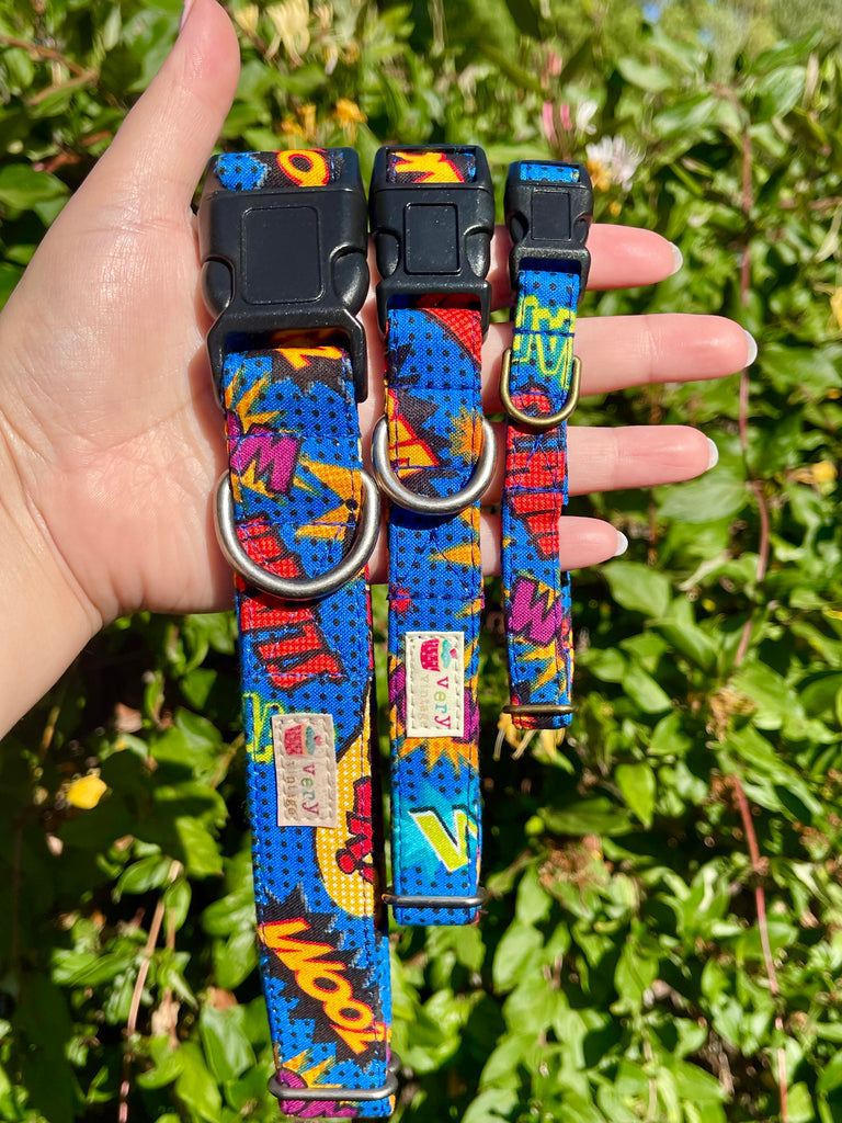 Colorful superhero print pet collar with black buckle and antique silver or antique brass hardware, shown with leafy green background.