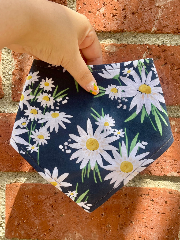 Navy blue bandana with daisy pattern held in front of brick wall, featuring yellow flower centers and clean stitching