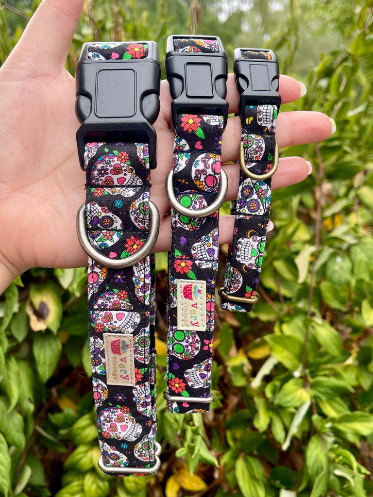 Hand holding collar with colorful sugar skull and flower print on black background, greenery backdrop