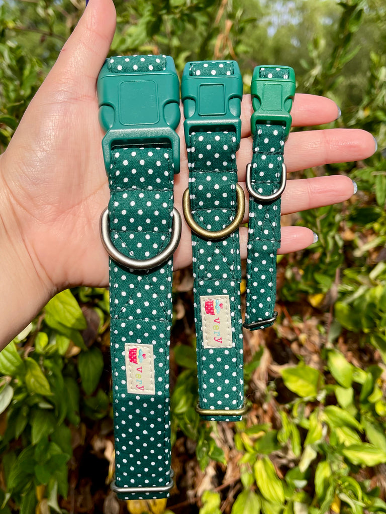 Forest green polka dot dog collar trio with antique brass and silver hardware in hand, shown outdoors with foliage background