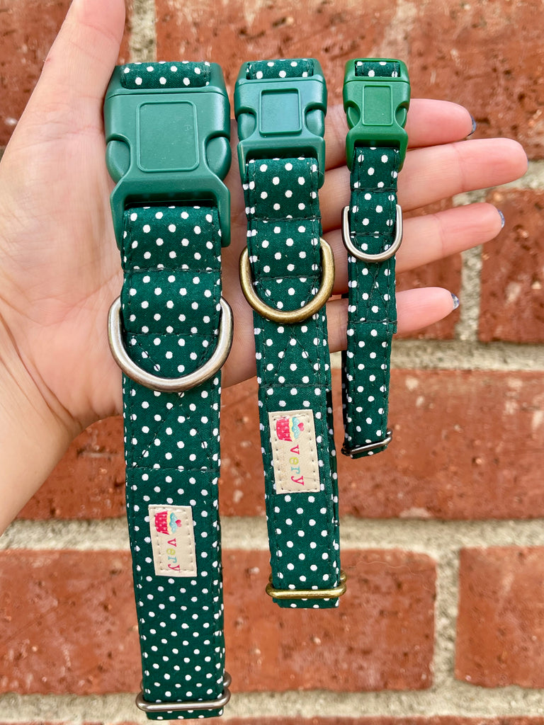 Hand holding forest green dog collar with white polka dots and green buckle against brick wall background