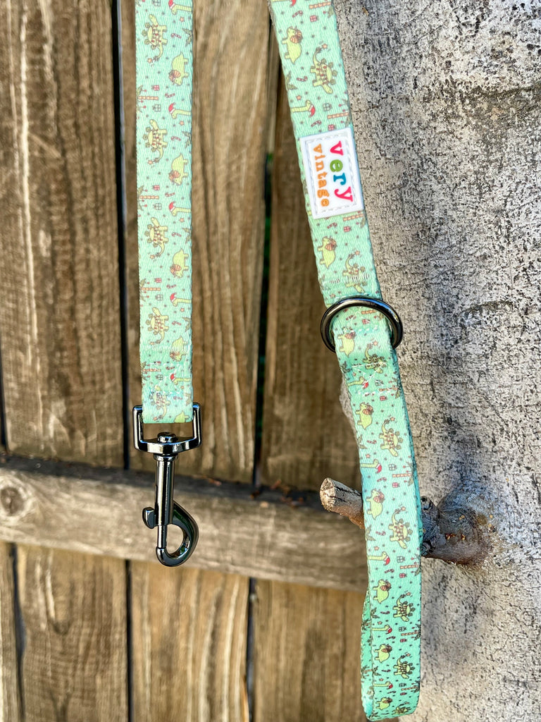 Festive Dinos dog leash with black metal clip hanging on wood fence