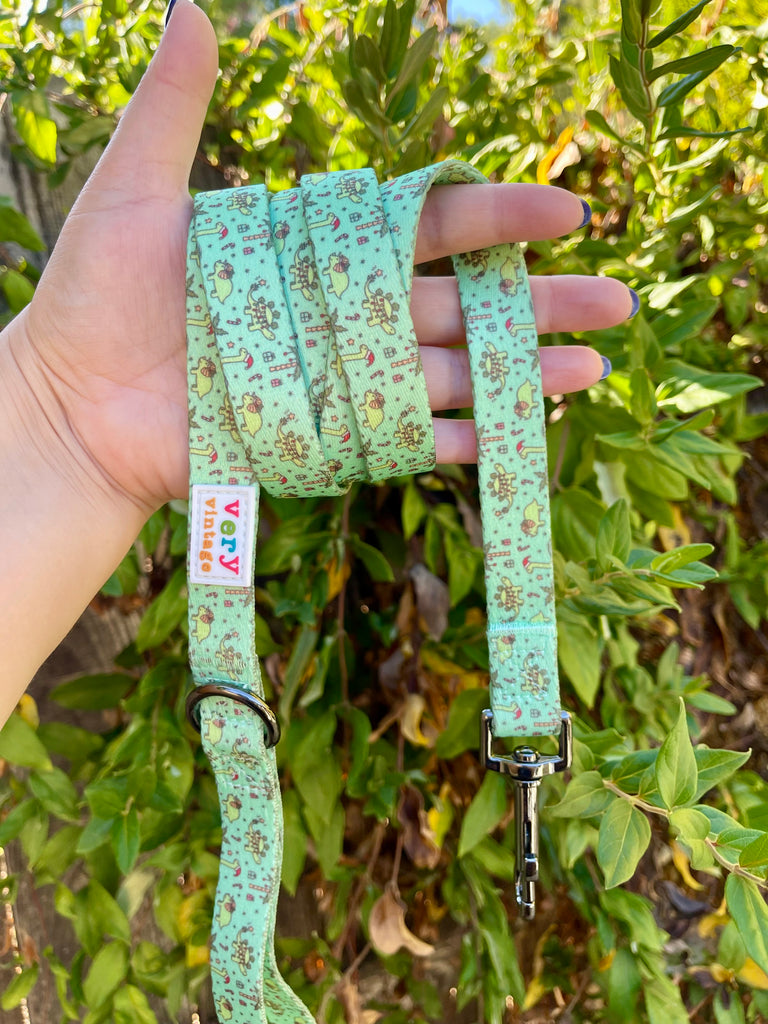 Hand holding Festive Dinos leash in sunlight, highlighting green fabric and holiday pattern