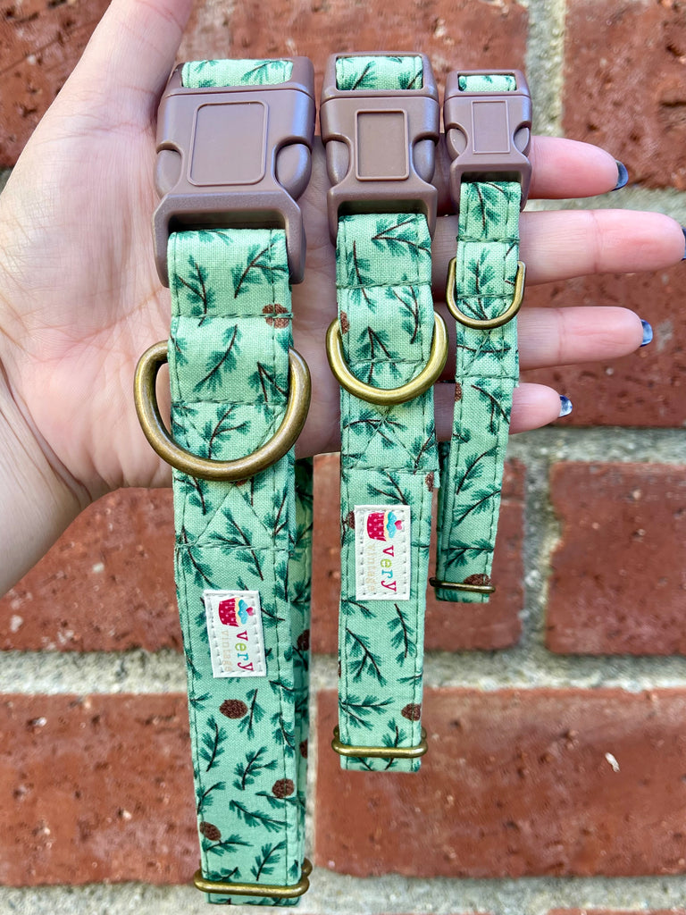 Hand holding three eco-friendly Forest Pines dog collars in front of brick wall – organic cotton green pine print collars for winter and Christmas pets