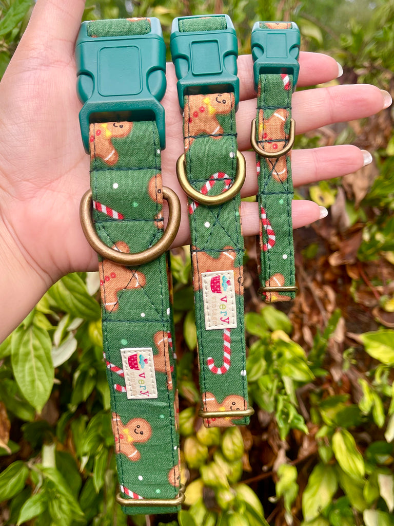 Hand holding three green holiday dog collars with gingerbread cookie and candy cane pattern against leafy background