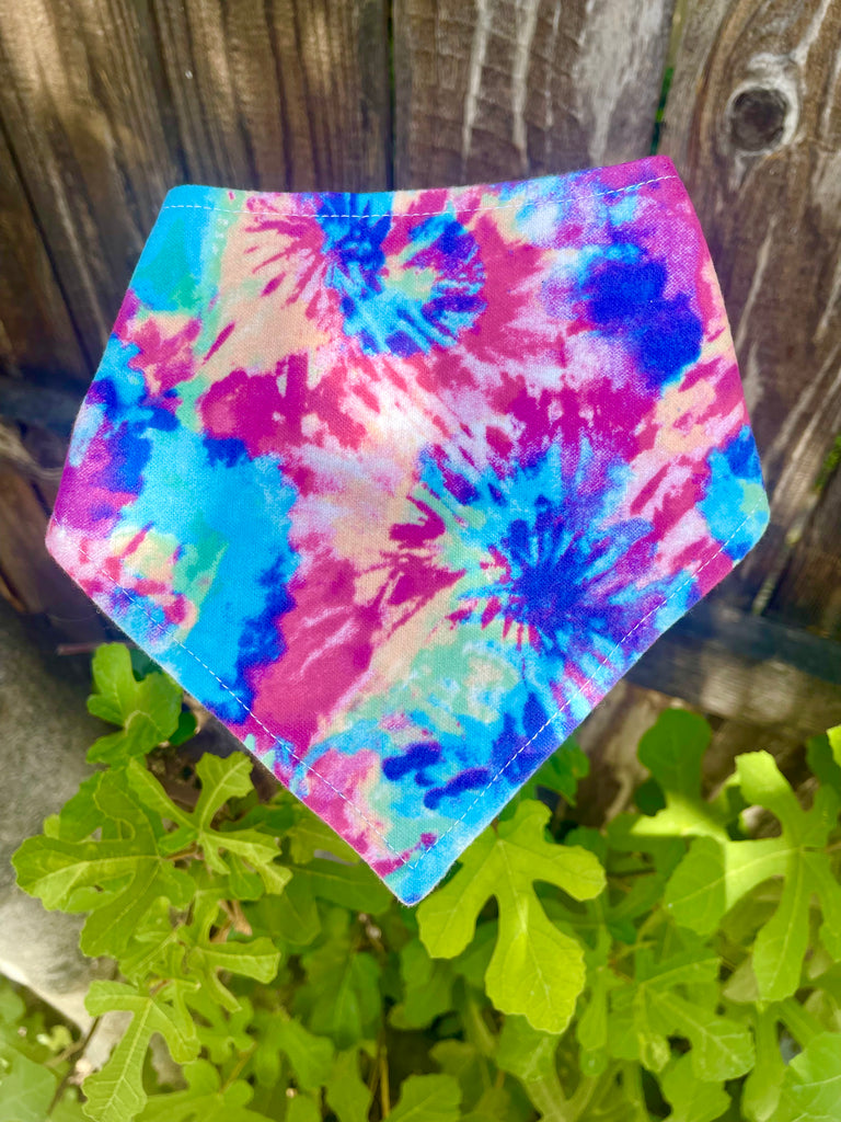 Colorful tie-dye bandana resting on green fig leaves with a rustic wood fence in the background