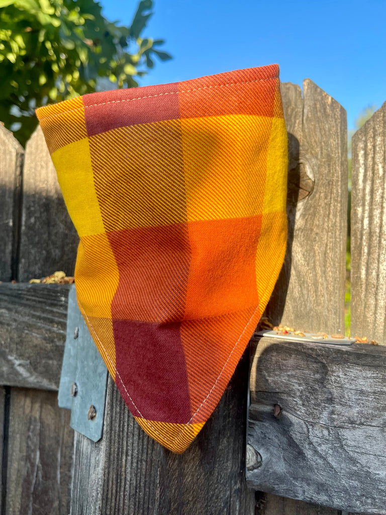 Autumn dog bandana with golden yellow and burnt orange plaid print draped on a fence
