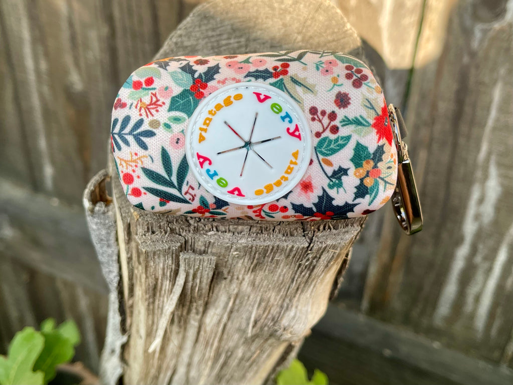 Close-up of the rubber dispenser port on the Holiday Floral poop bag holder, surrounded by a festive botanical pattern