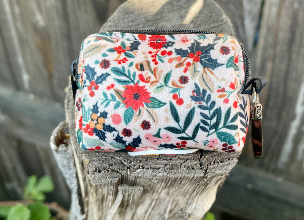 Dog poop bag holder resting on a rustic wood stump, showcasing a winter floral pattern with red and green details