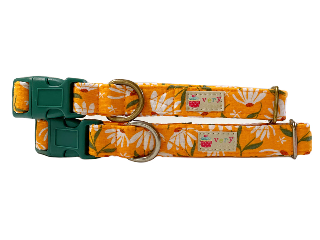 Close-up view of a mustard gold dog collar with white daisy flowers, showcasing the vibrant floral pattern on organic cotton fabric. The collar features durable hardware and a bright, spring-inspired design.