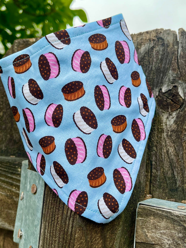 Light blue dog bandana with chocolate and strawberry ice cream sandwich print, styled draped over rustic wood fence, outdoors. Handmade in Los Angeles, California.