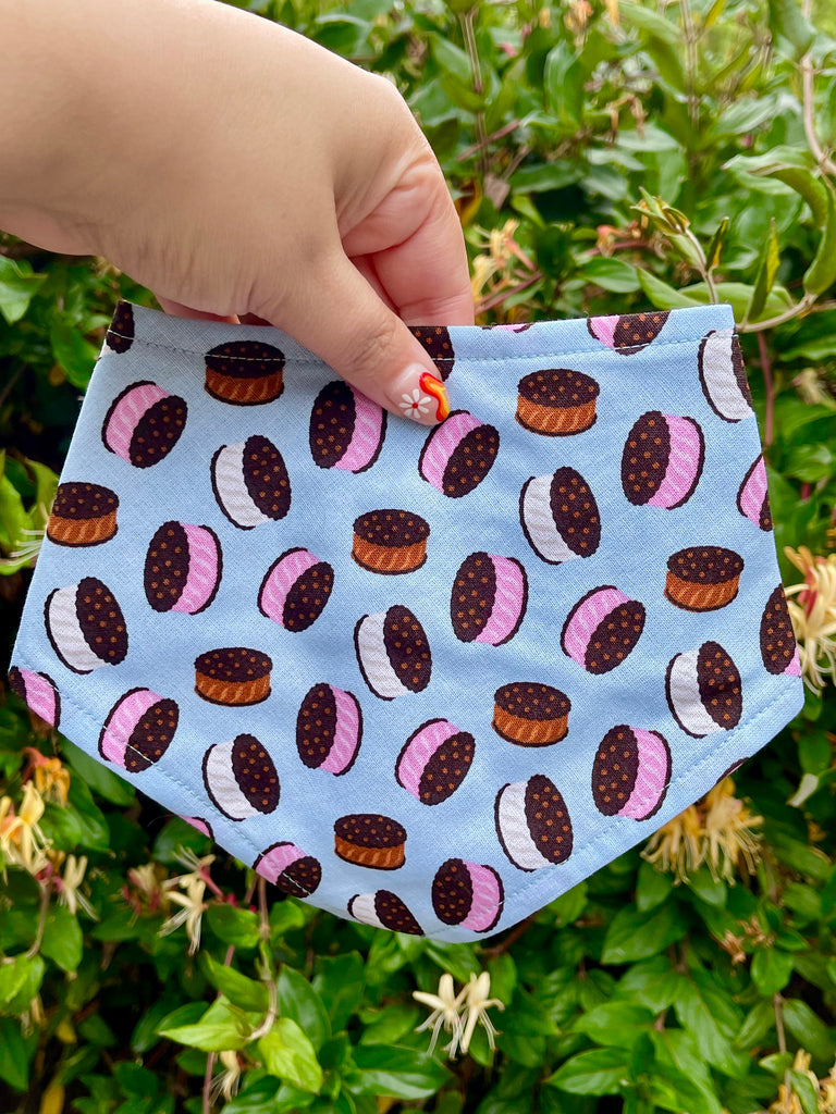 Close-up of light blue bandana with ice cream sandwiches, held by hand with colorful manicure, green garden background.