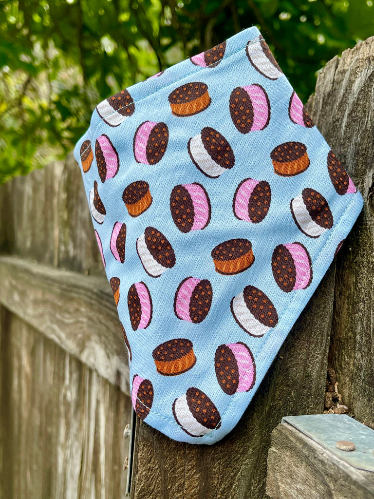 Side angle of ice cream sandwich print bandana on wood fence, capturing playful dessert pattern on pastel blue fabric. Perfect for summer!