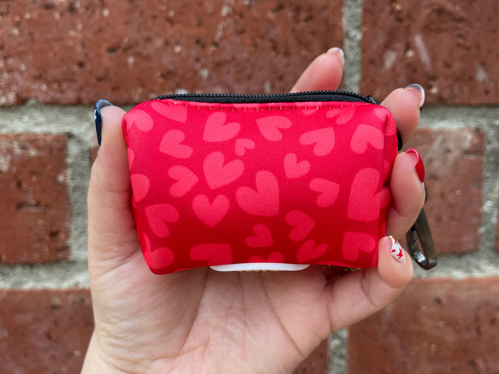 Poop bag holder with pink heart design shown against red brick wall background