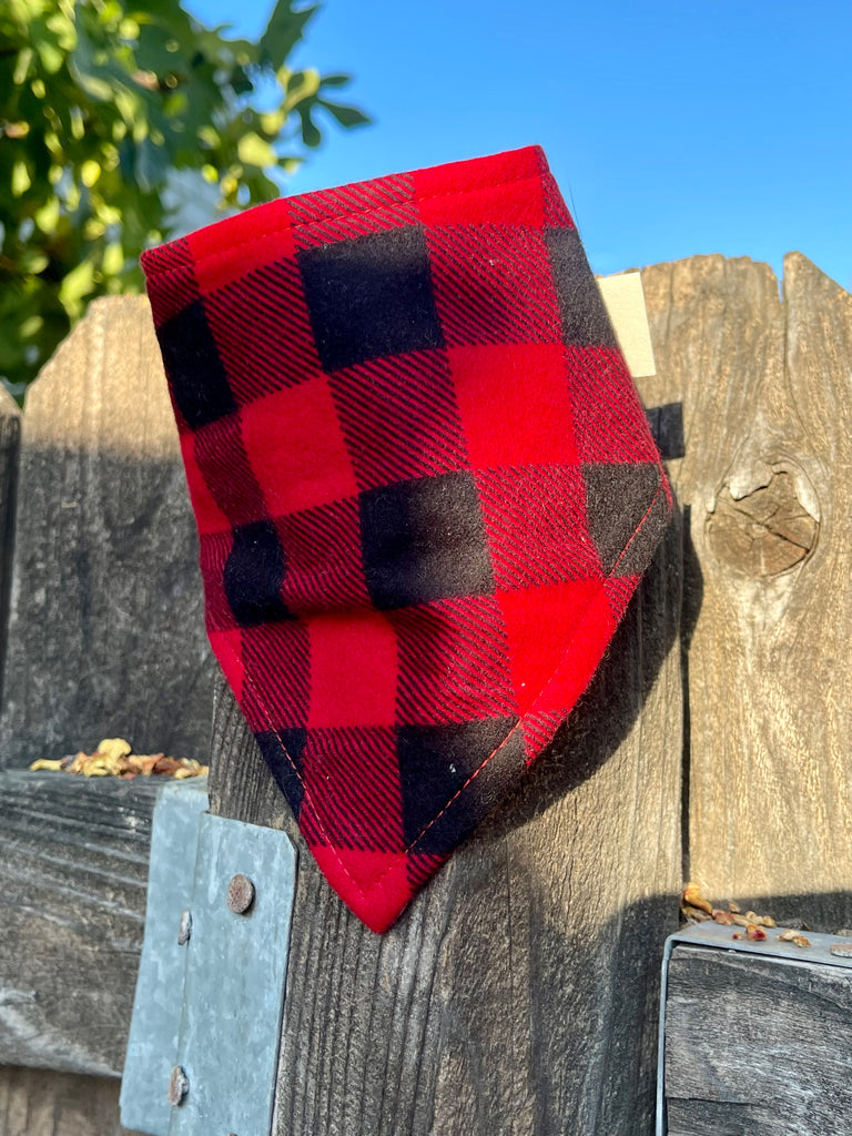 Buffalo plaid bandana resting on a wooden fence in warm light. Cozy flannel pattern in red and black, perfect for winter wear