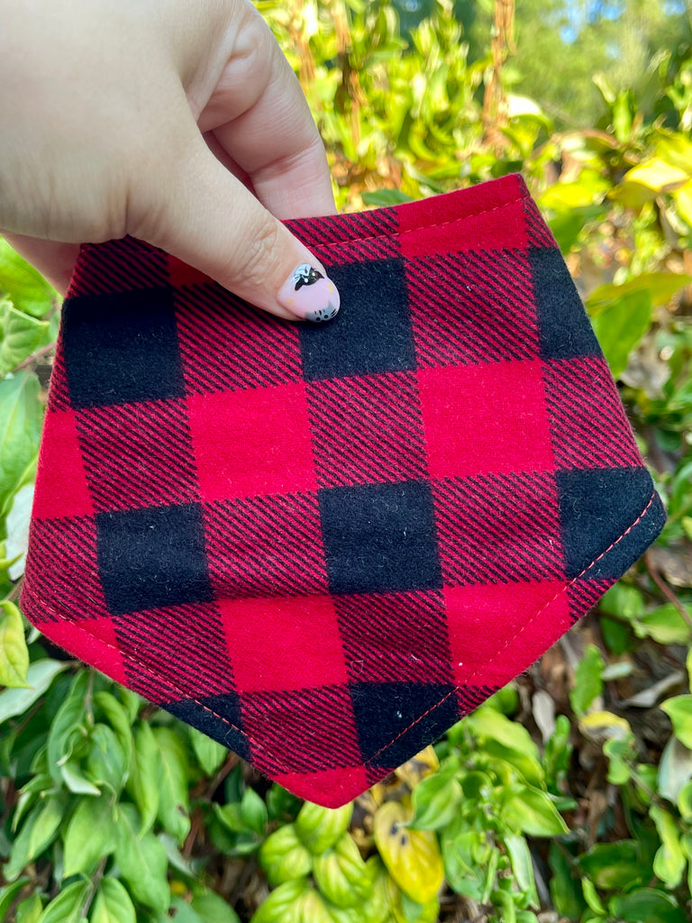 Lumberjack bandana held up to leafy greenery. Classic red-and-black buffalo plaid print adds rustic charm