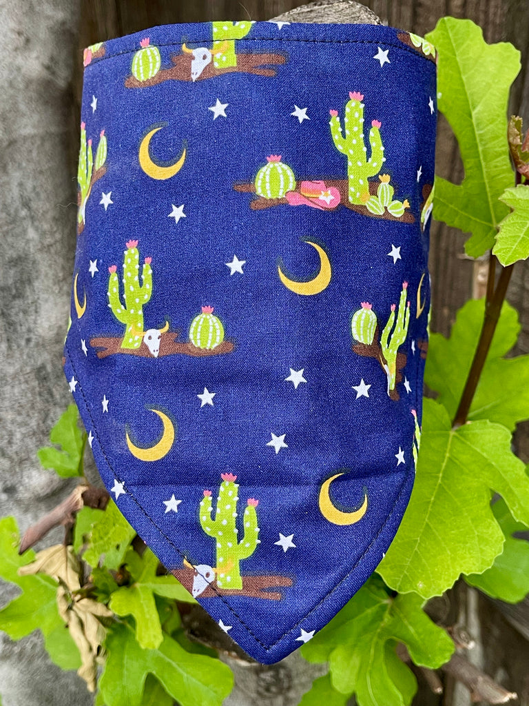 Close-up of folded cactus dog bandana featuring cow skulls, moons, and desert blooms on deep navy cotton.