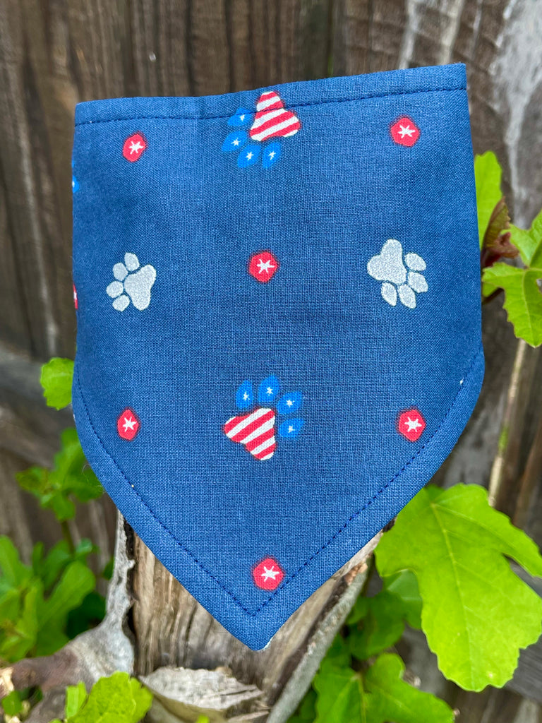 Close up view of red, white, and blue paw print fabric on eco-friendly dog bandana. The paws are in silver and red, white and blue, with red polka dots.