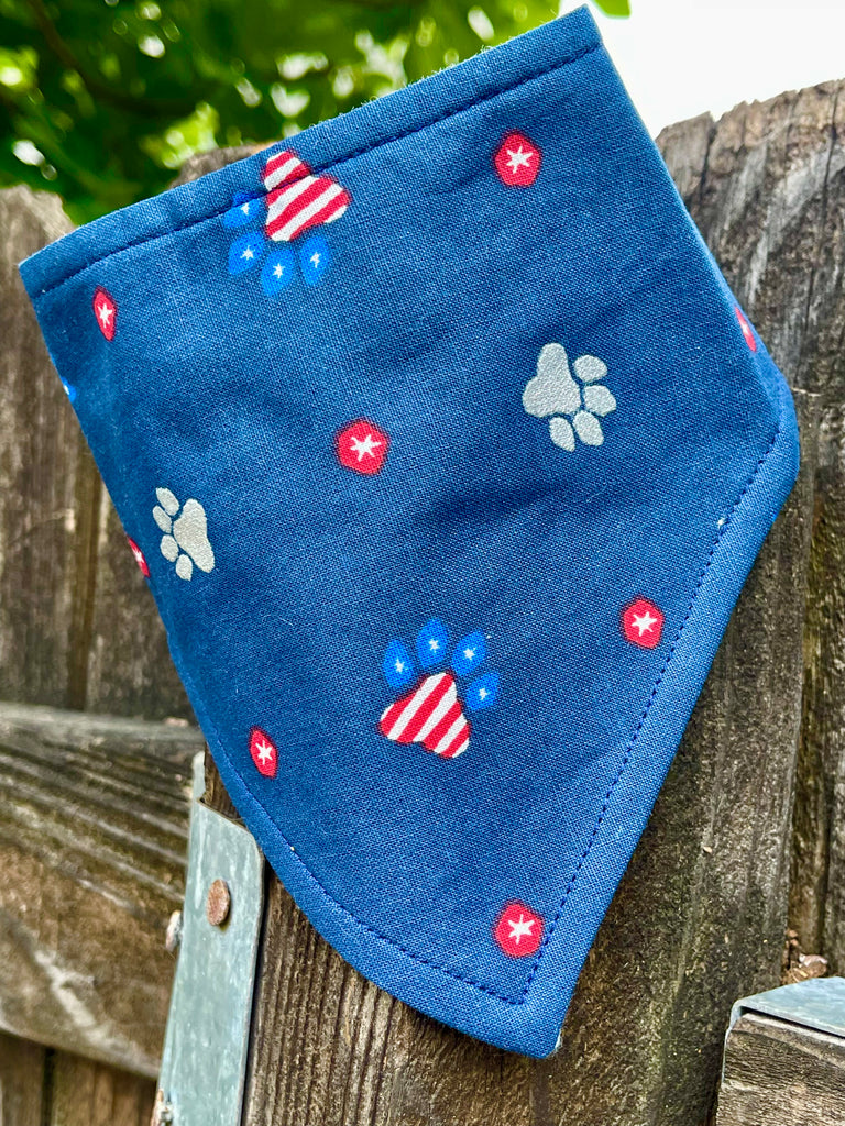 Snap on patriotic paw print bandana displayed on a fence, emphasizing the bold red, white, and blue color scheme, ideal for Fourth of July or Memorial Day.