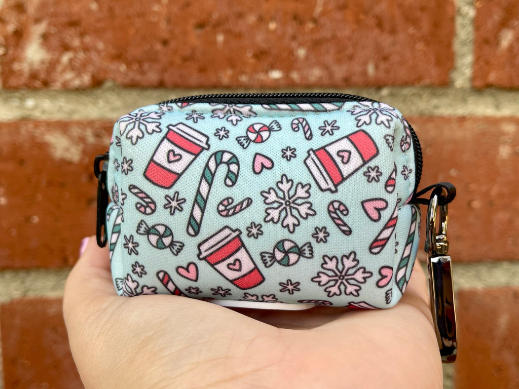 Peppermint Mocha poop bag holder with holiday coffee cups, candy canes, and snowflakes on a mint green background, shown in hand against red brick.