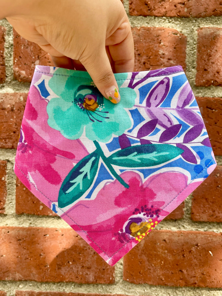 Snap dog bandana with bold floral design held in front of brick wall, showing colorful petals and detailed stitching