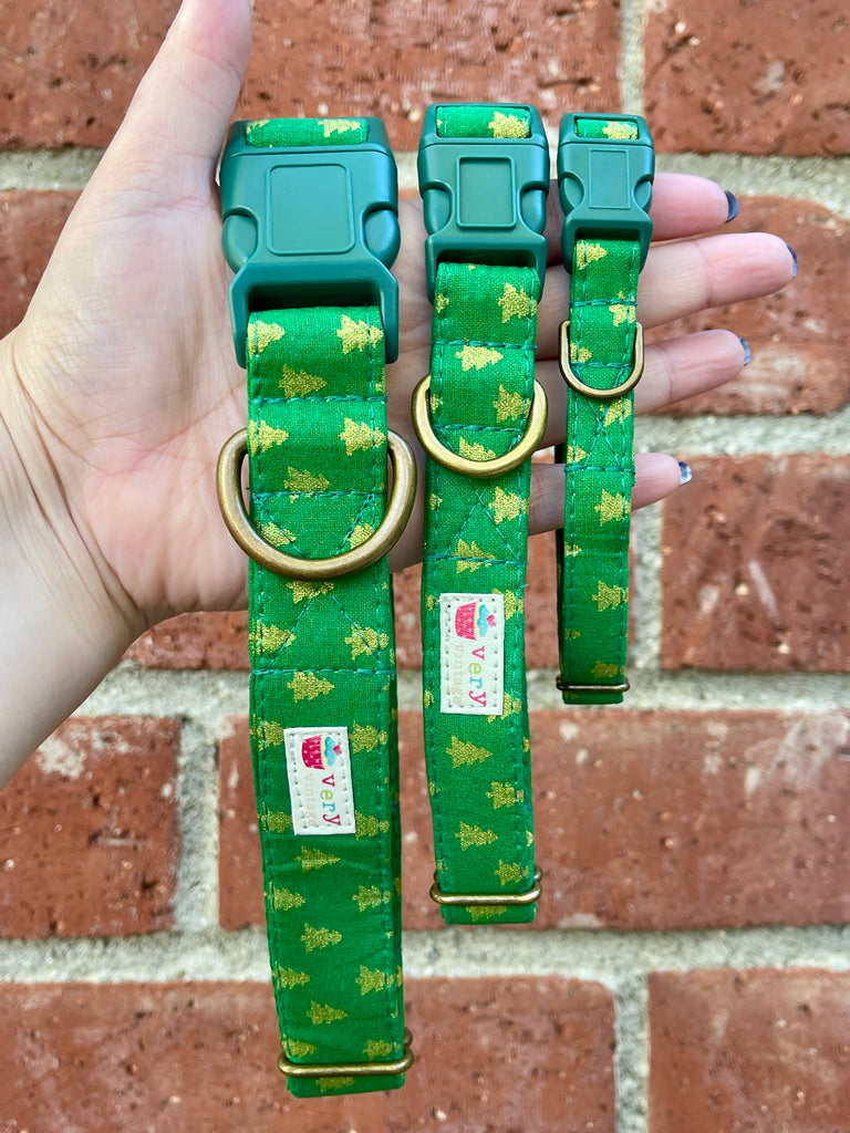 Hand holding three eco-friendly green holiday dog collars in front of brick wall – organic cotton Christmas tree collars handmade in the USA