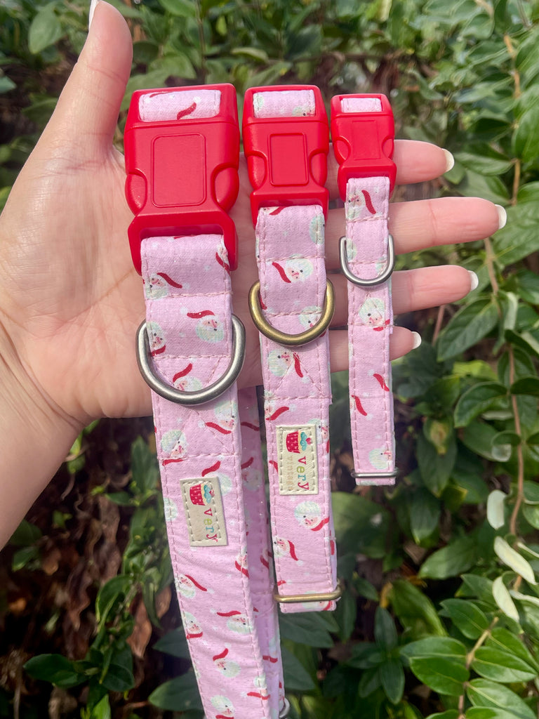 Hand holding pink Santa print collars with bright red buckles in sunny garden greenery background