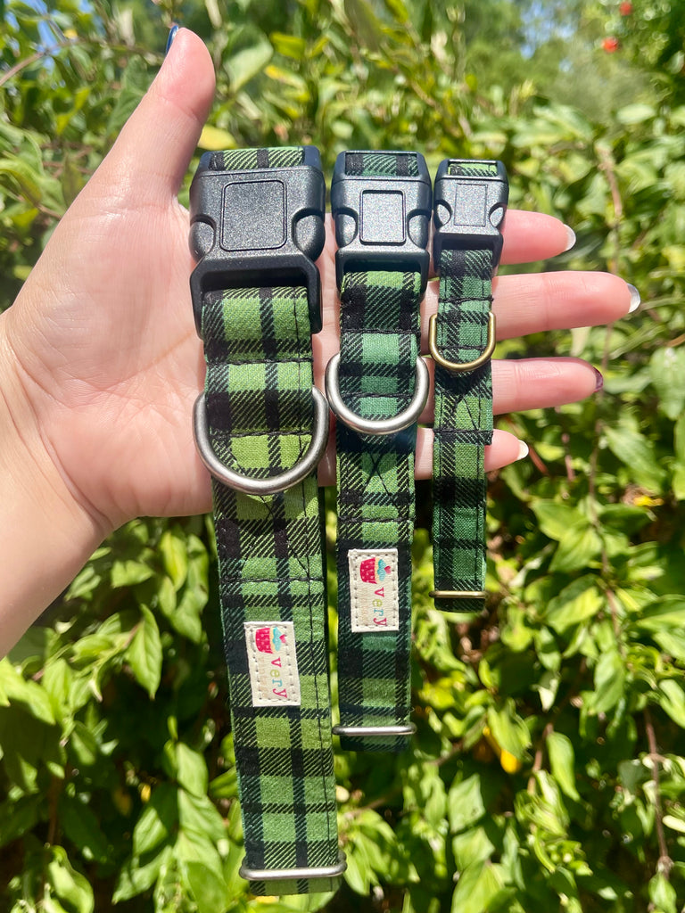 Green and black plaid dog collars in three sizes, held in hand outdoors with leafy green background