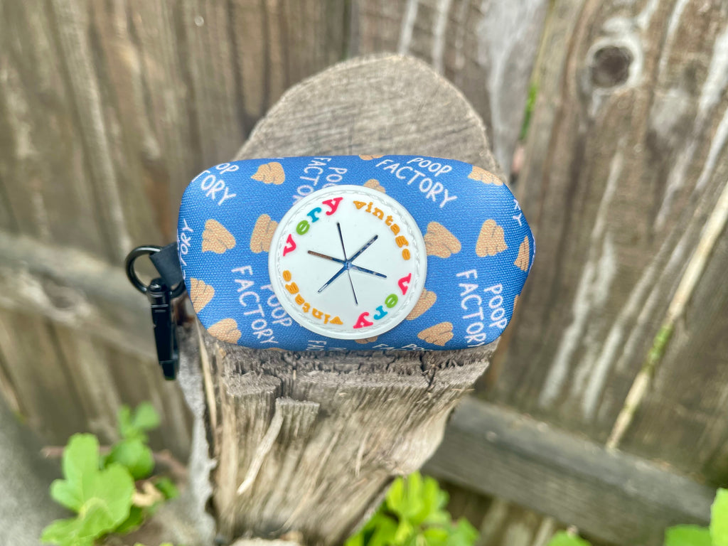 Side logo view of poop pouch showing dispenser opening, wood background.