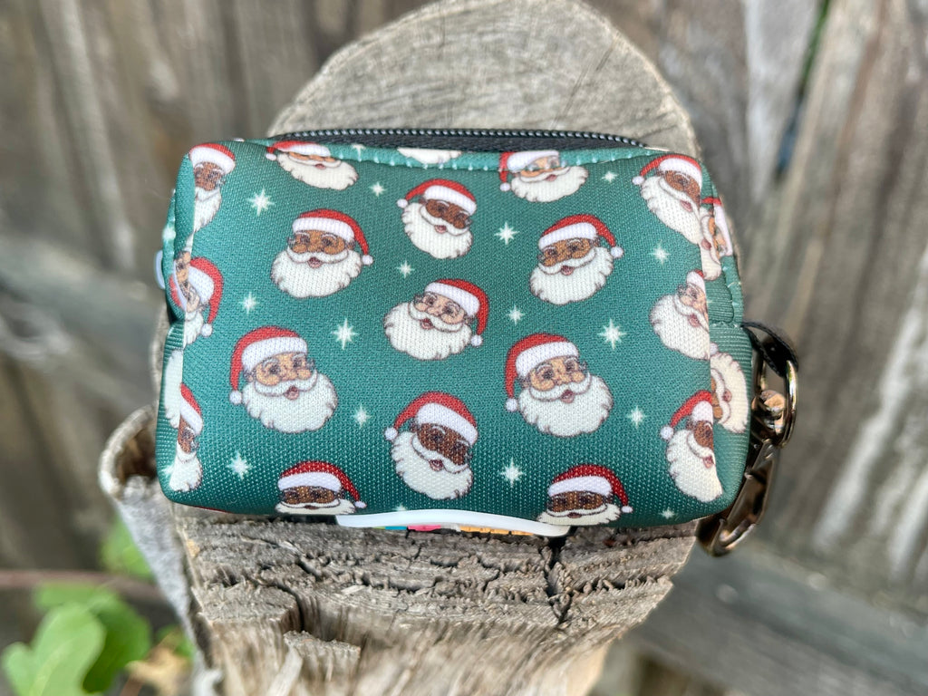 Green poop bag holder with diverse Santa faces, photographed on wooden stump with rustic fence backdrop