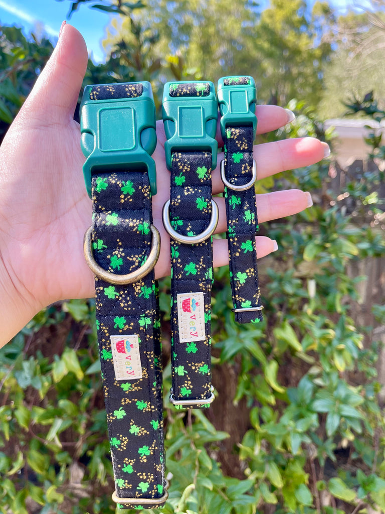 Three dog collars with green and black patterns held by a hand against a green outdoor background.